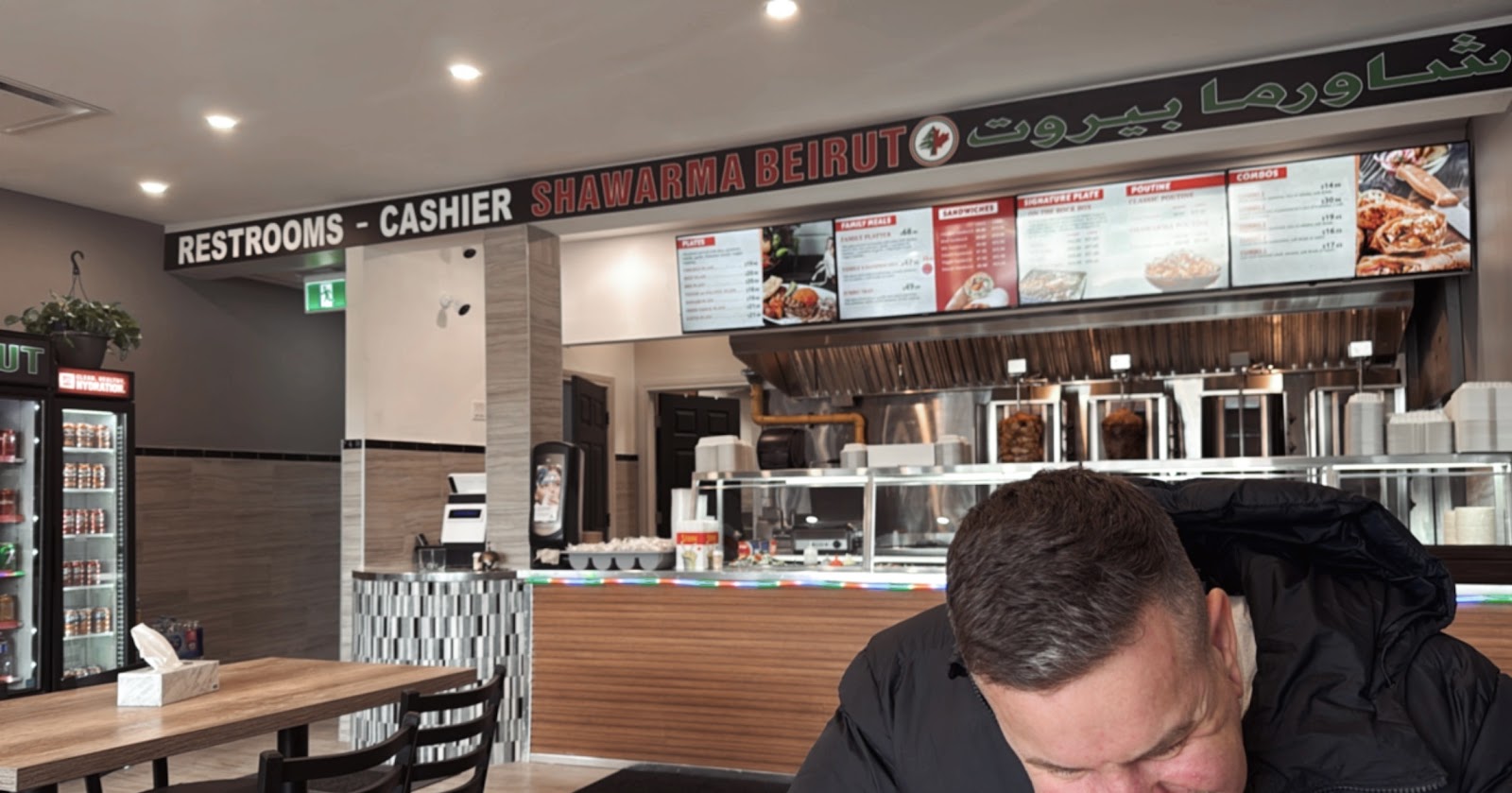Wide interior view of Shawarma Beirut dining room and ordering counter with digital menu boards, beverage fridge, and signage reading RESTROOMS - CASHIER