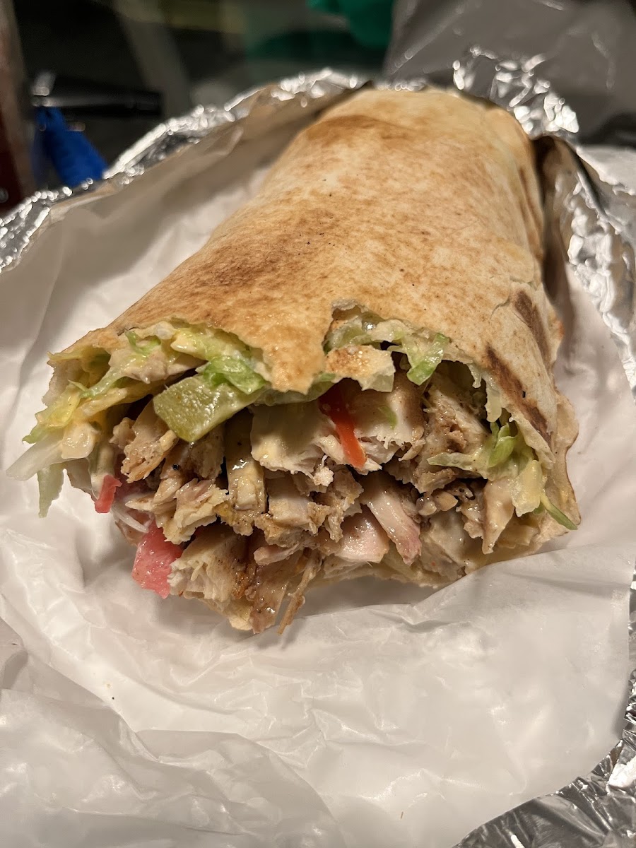 A chicken shawarma wrap cut open on foil showing chicken, lettuce and tomato