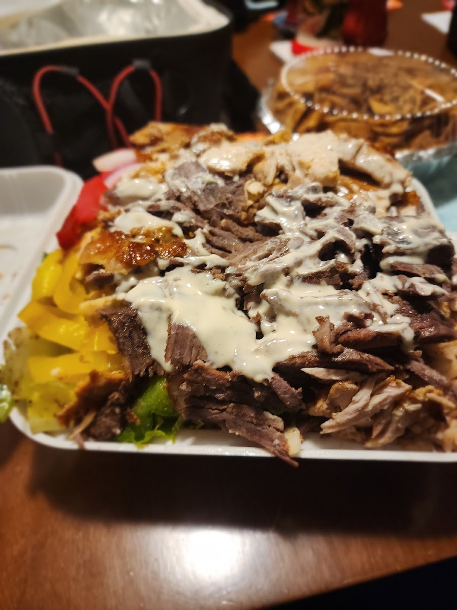 A loaded shawarma platter with meat, garlic sauce and peppers in a takeout tray