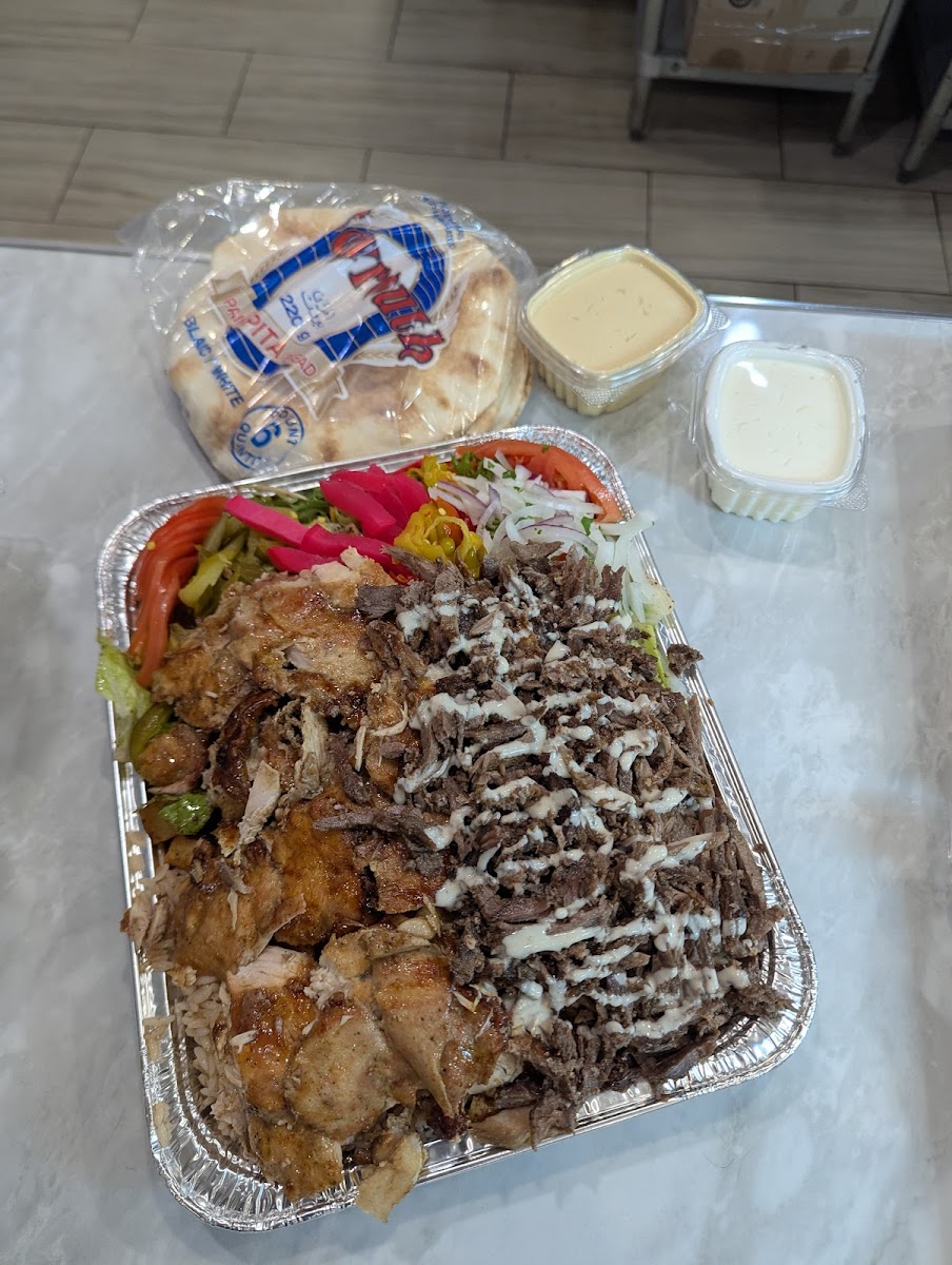 A shawarma platter with garlic-drizzled meat and peppers, a wrapped pita and sauce cups